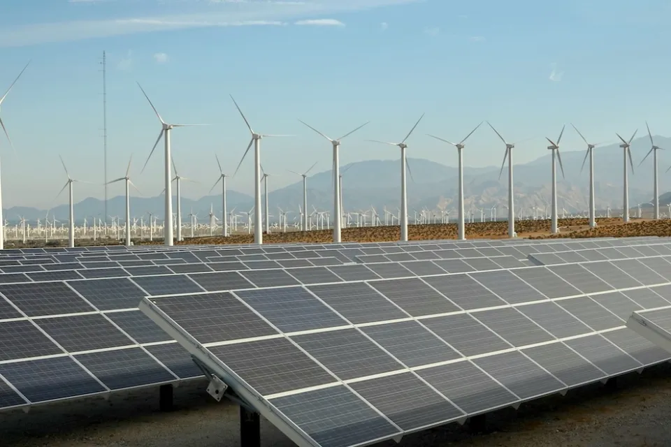 Large solar panel installation and wind turbines with Southern California desert mountains in background.